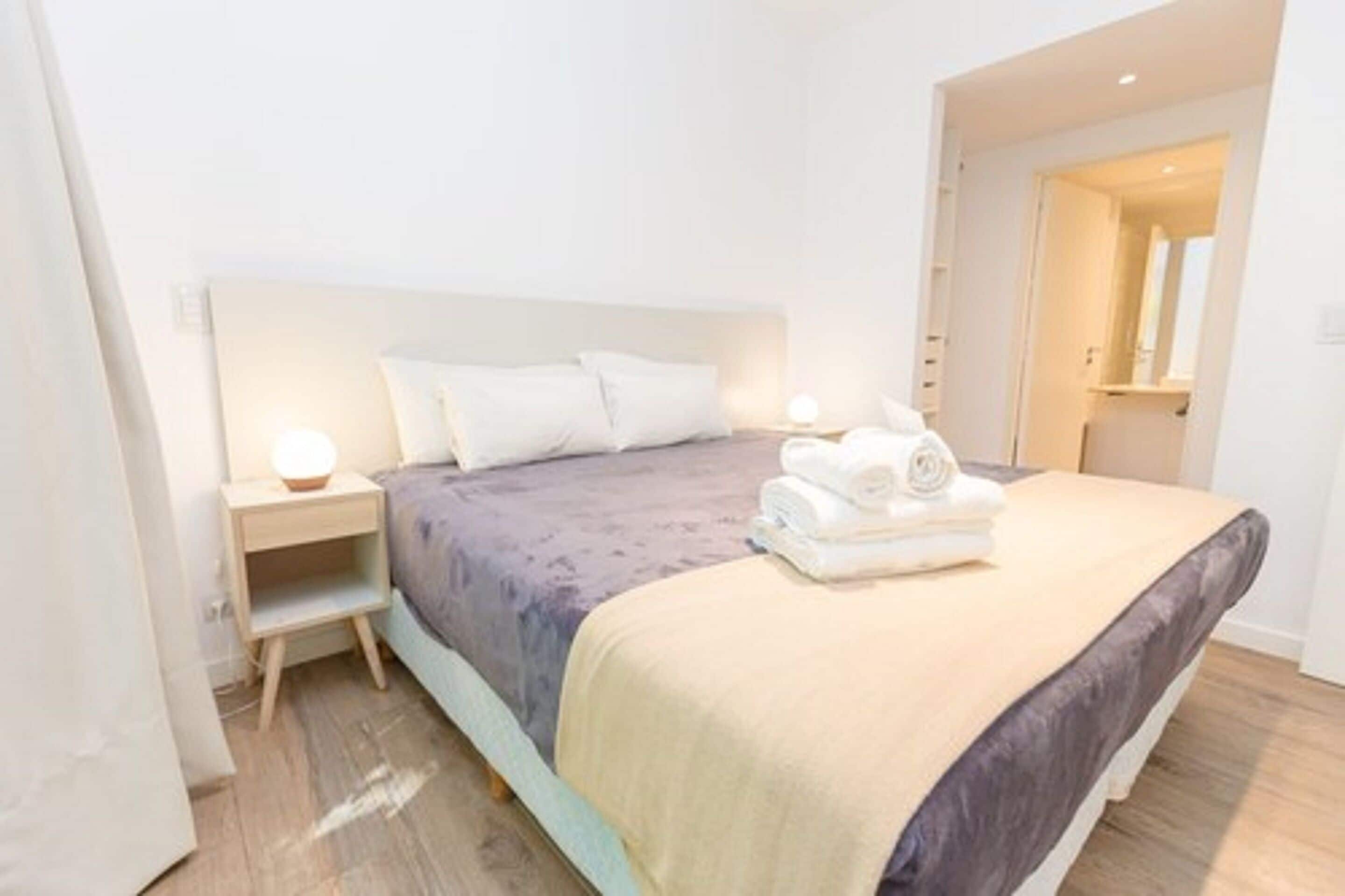 Une chambre à coucher bien rangée, avec un lit, des tables de chevet et une porte de salle de bain visible.