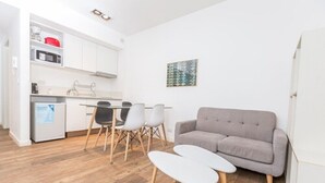 A modern kitchen with white cabinets, a dining table with chairs, a grey sofa, and a small white table. - Babel Belgrano (Buenos Aires)
