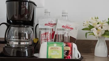 Una cafetera, dos botellas de agua, una bolsita de té y un florero con flores sobre una bandeja.