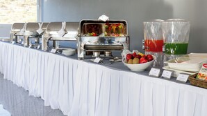 Un buffet avec plusieurs présentoirs de nourriture, un saladier de fruits et des plats de service étiquetés.