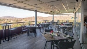 Un espace de restauration en plein air avec des tables et des chaises, une vue sur le paysage désertique et une partie abritée dotée d’un mur en verre.