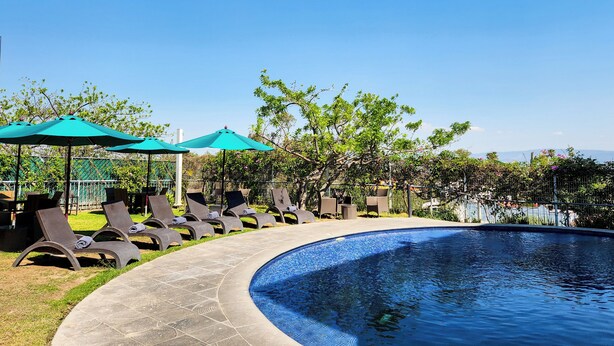 Un espace aménagé au bord de la piscine, avec des chaises longues et des parasols, entouré de verdure et surplombé d’un ciel dégagé.