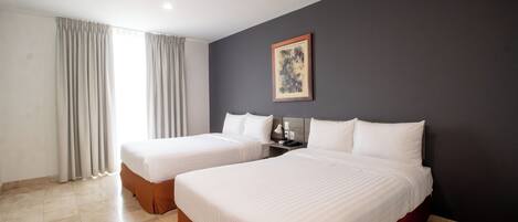 A hotel room with two beds, a dark accent wall, a painting, and a window with curtains.