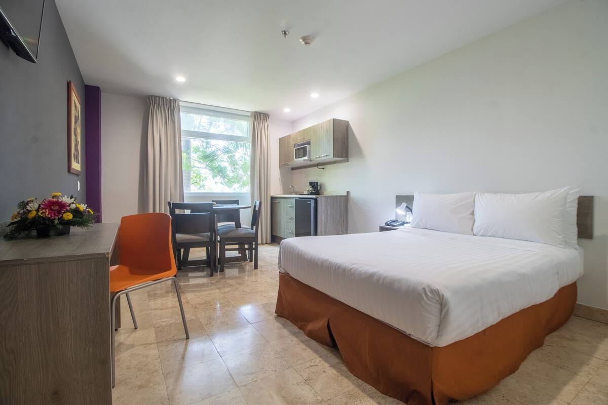 Una habitación de hotel con cama, escritorio, silla y una pequeña kitchenette.