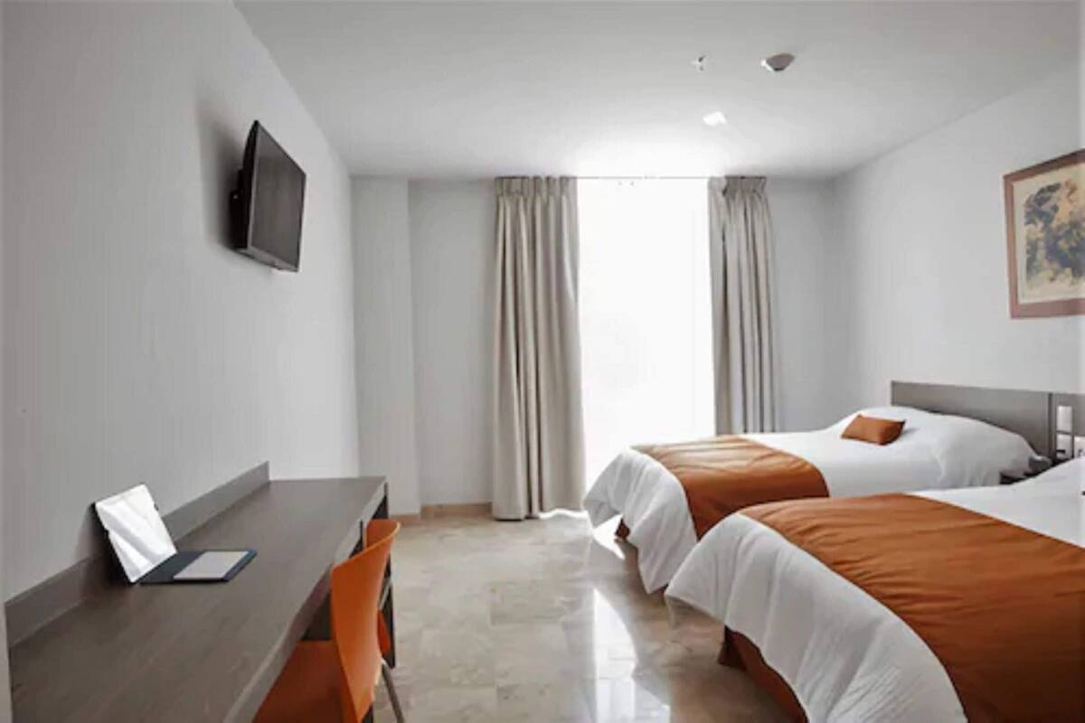 Habitación de hotel con dos camas, un escritorio, una silla, un televisor y una ventana con cortinas.