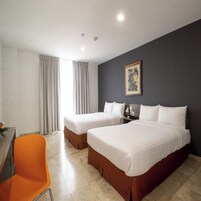 Une chambre d’hôtel avec deux lits, un bureau, une chaise orange et un tableau au mur.