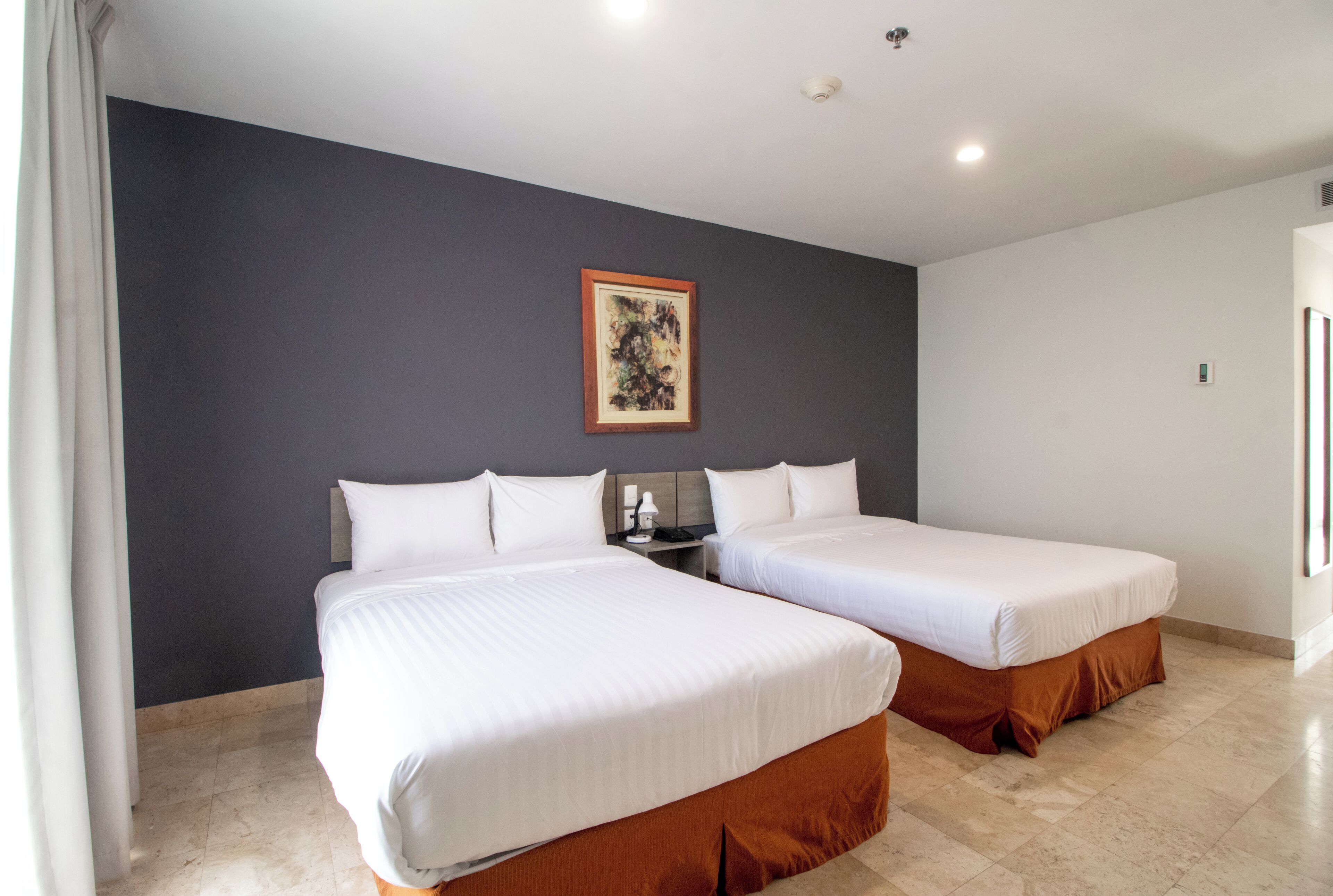 Una habitación de hotel con dos camas, una pared oscura y un cuadro.