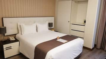 Una habitación de hotel con una cama grande, una mesita de noche con lámpara, teléfono y armario.