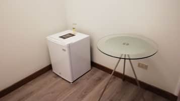 Una habitación pequeña con un refrigerador blanco, una mesa de vidrio sobre cuatro patas, y piso de madera.