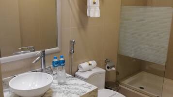 Un baño moderno con lavamanos de mármol, inodoro, ducha con mampara de vidrio y toallero con toallas dobladas.