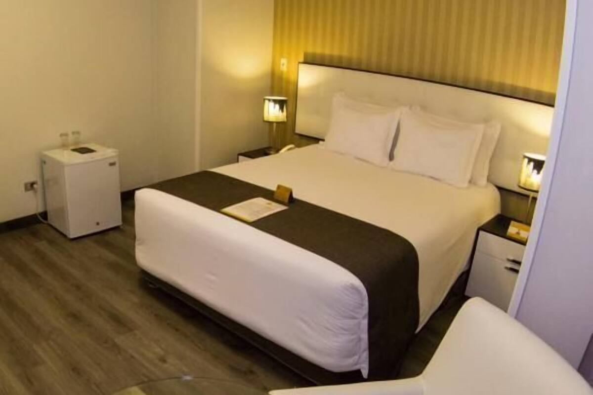 Une chambre d’hôtel comprenant un lit, des tables de chevet, une chaise, une petite table et un radiateur fixé au mur.