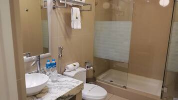 A bathroom with a marble sink, a toilet, a glass-enclosed shower, and a towel rack with folded towels.
