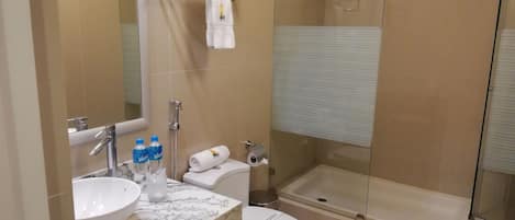 Un baño con lavamanos de mármol, inodoro, ducha con mampara de vidrio y toallero con toallas dobladas.