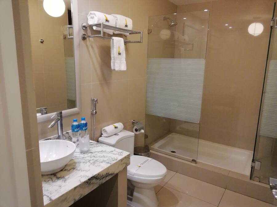 A bathroom with a marble sink, a toilet, a glass-enclosed shower, and a towel rack with folded towels.