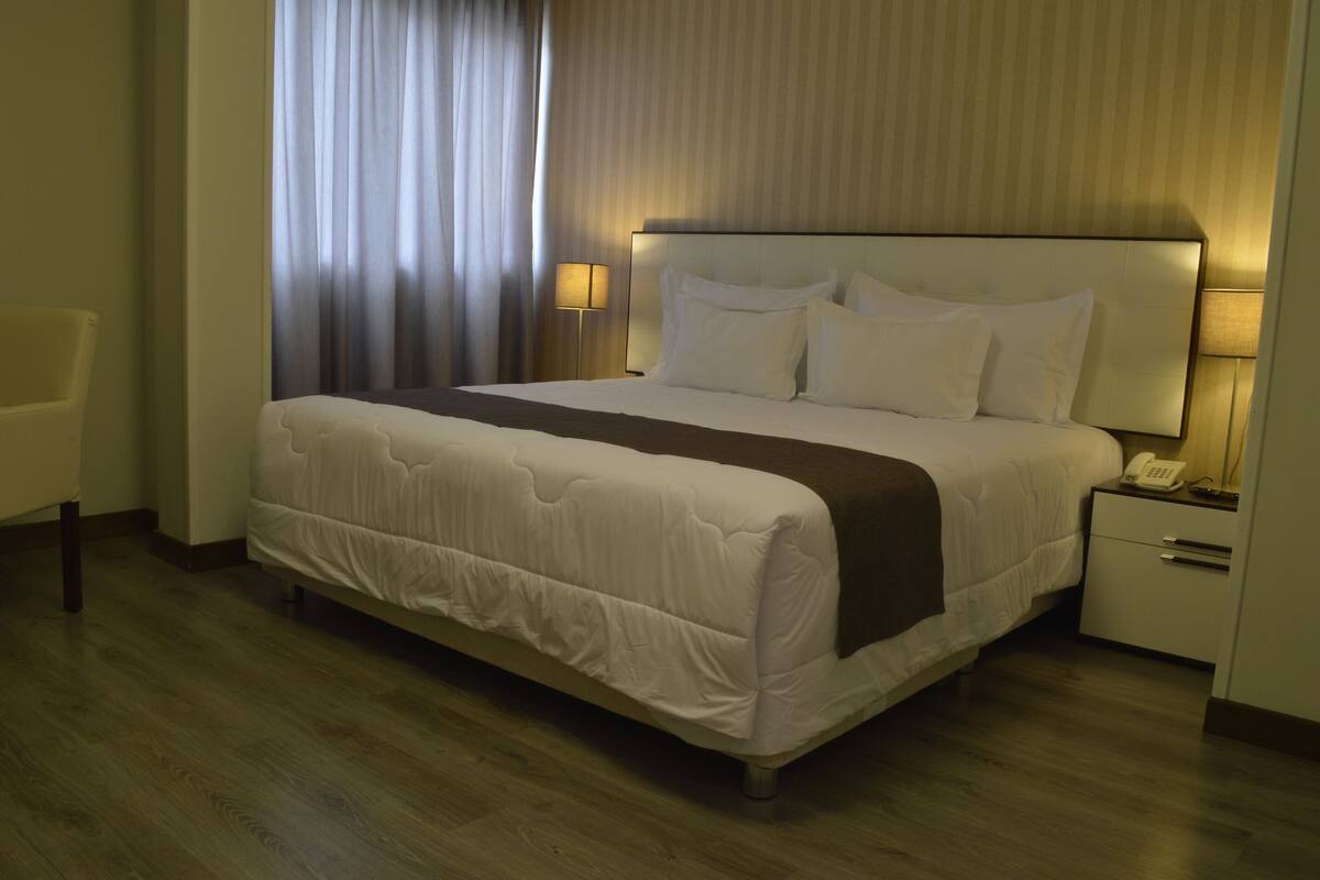 Une chambre d’hôtel avec un grand lit, une table de chevet avec une lampe et une chaise.