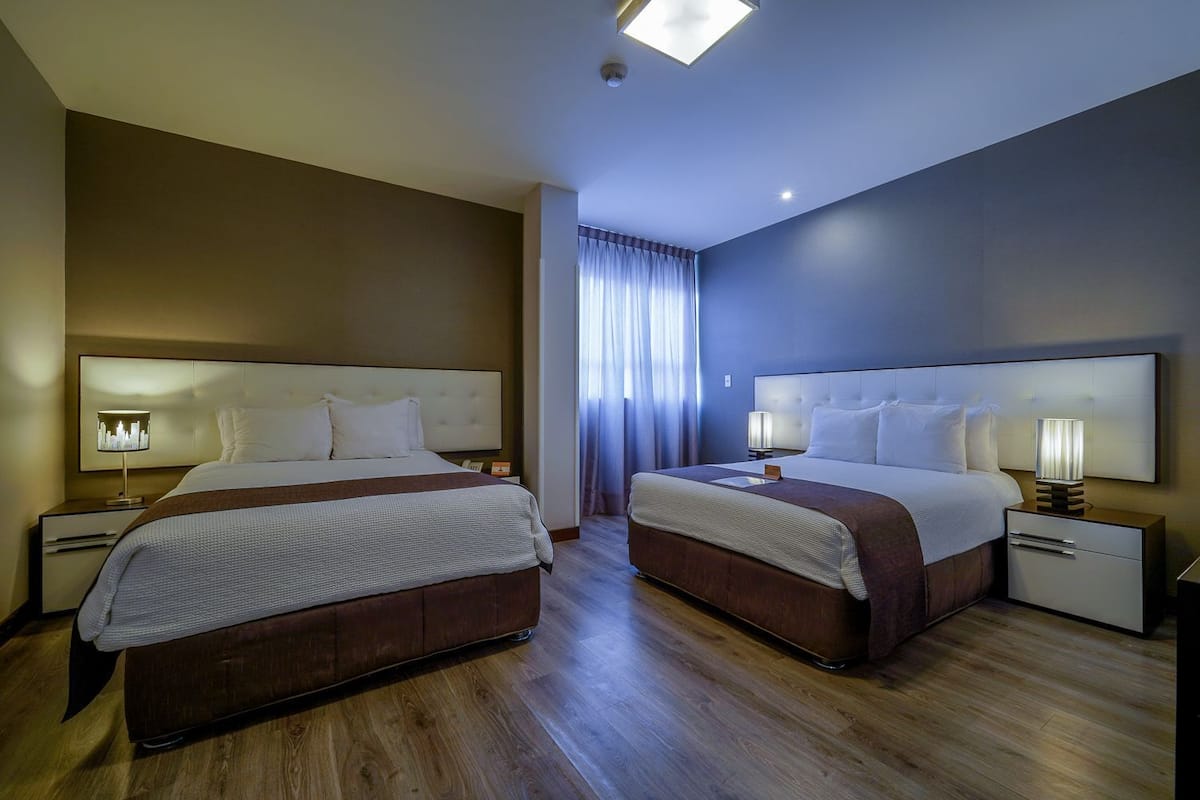 Une chambre d’hôtel avec deux lits, deux tables de chevet, une grande fenêtre avec des rideaux et un luminaire au plafond.