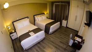 Habitación de hotel con dos camas, un escritorio con silla, un minibar y una televisión.