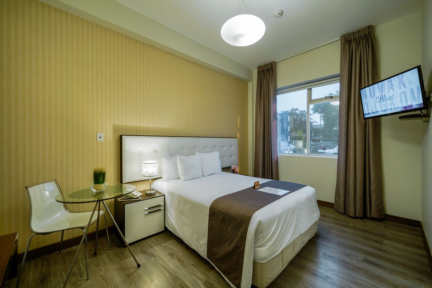 Ein Hotelzimmer mit Bett, Nachttisch, Lampe, Stuhl und Fernseher an der Wand.