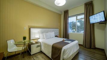 A hotel room with a bed, bedside table, lamp, chair, and a TV on the wall.