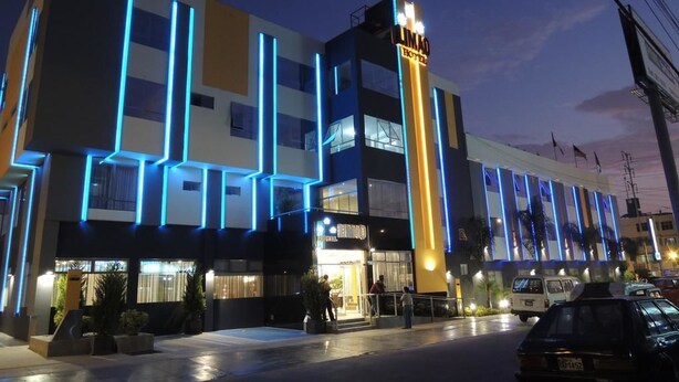 Un hotel moderno con un llamativo letrero vertical, varios balcones y un área de entrada bien iluminada.