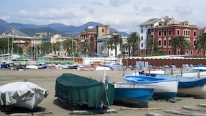 A marina with boats docked, a sandy beach, and buildings in the background.