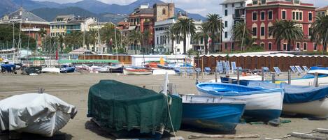 A marina with boats docked, a sandy beach, and buildings in the background.