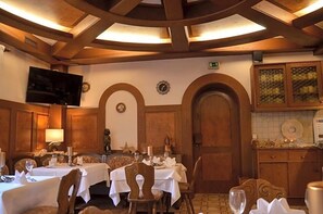 A restaurant with wooden decor, tables set with white tablecloths, and a television mounted on the wall.