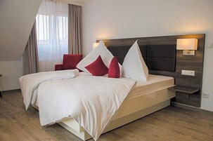 Una habitación de hotel moderna con una cama grande, una silla roja, una mesita de noche y una lámpara de pared.