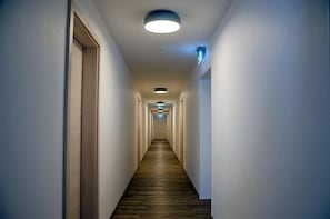 A long, narrow hallway with wooden flooring and white walls, leading to a door at the end.