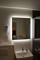 Un baño con lavamanos, espejo y secador de pelo fijado a la pared.