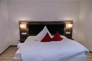 A hotel room with a large bed, two bedside lamps, and a dark headboard.