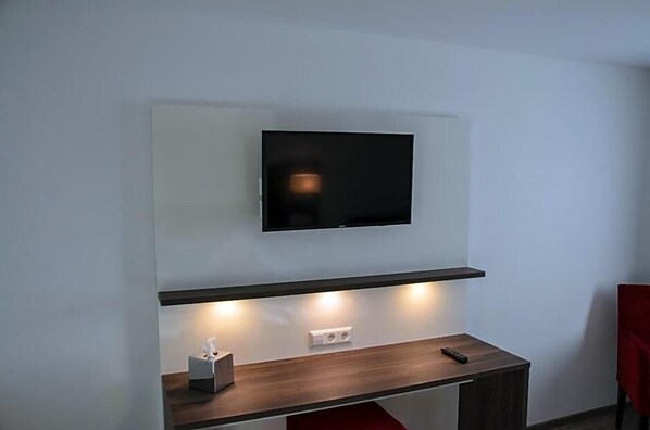 A modern room with a mounted TV, a wooden desk, and a red chair.