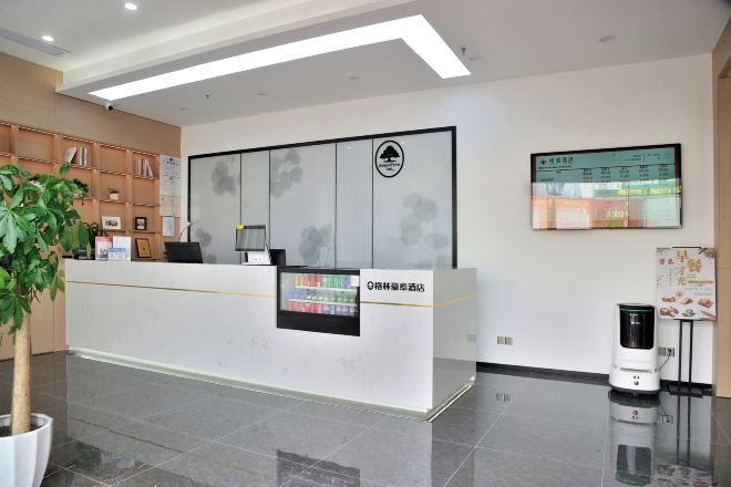 Un mostrador de recepción con una pantalla digital, una planta y un robot en un vestíbulo moderno.