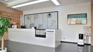 Un mostrador de recepción con una pantalla digital, una planta y un robot en un vestíbulo moderno.