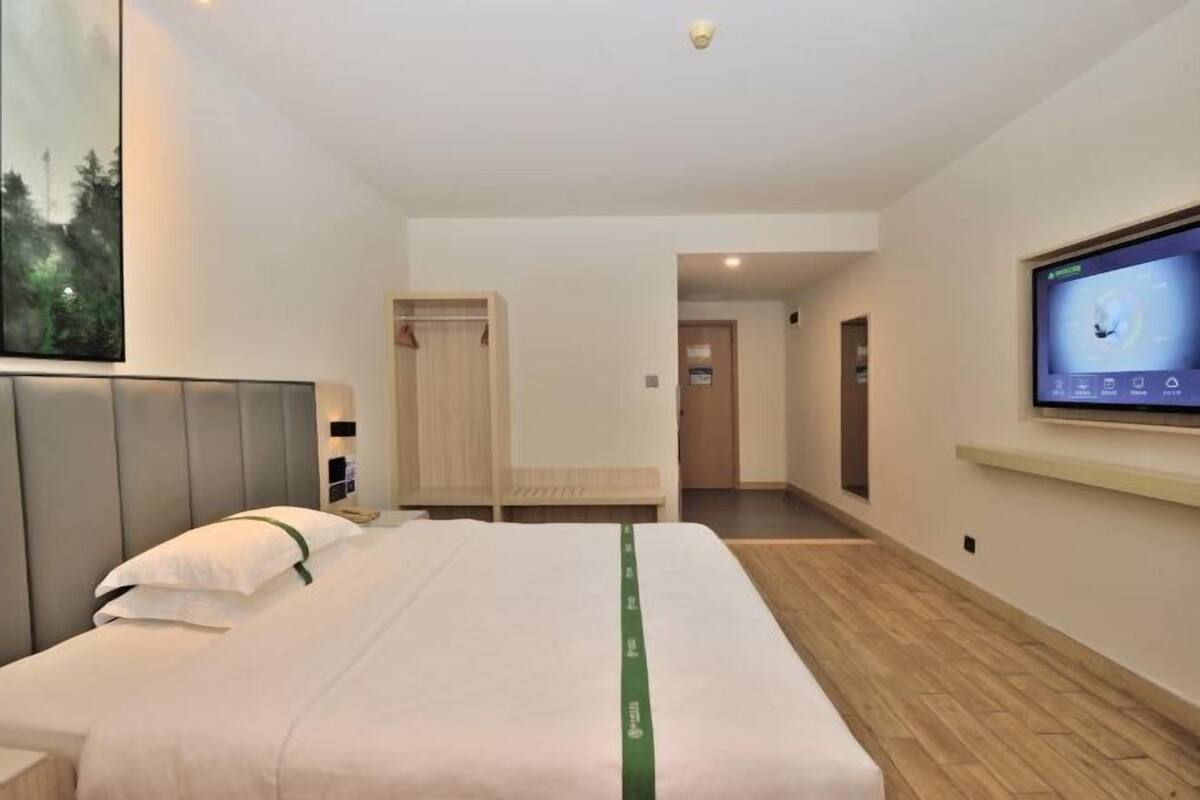 A hotel room with a bed, a television, a wooden floor, and a view of the outdoors.