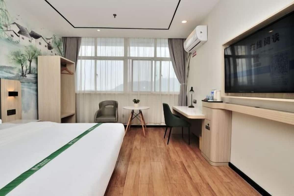 A hotel room with a bed, desk, chairs, and a large window.