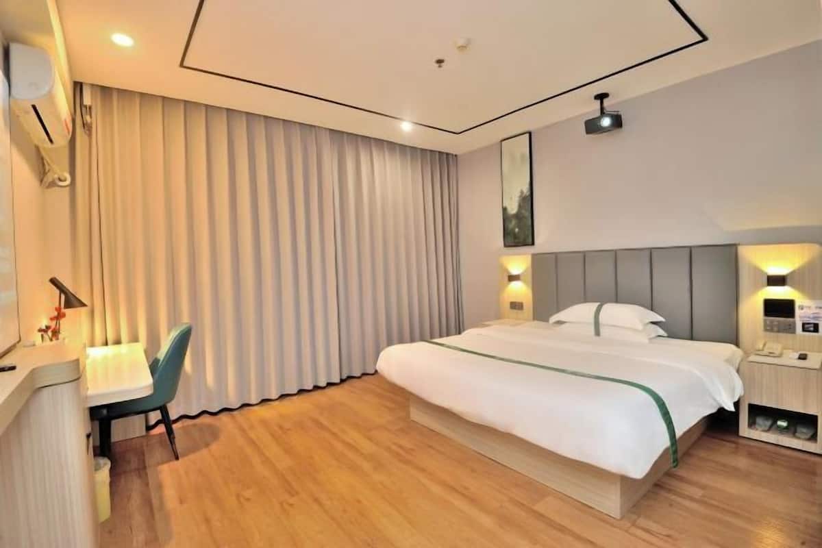 A hotel room with a bed, bedside table, lamp, and a desk with a chair.