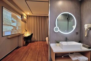 A modern hotel room with a wooden floor, a large flat-screen TV, a round mirror with a light, and a white sink. - GreenTreen Alliance Hotel Suzhou Mudu Town Jinshan Road Branch (Suzhou)