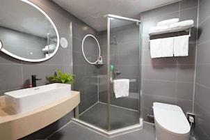 Un baño moderno con ducha envuelta en vidrio, un espejo grande, un lavabo y un inodoro.