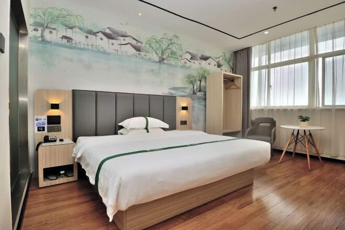 A hotel room with a bed, bedside tables, a chair, a small table, and a mural on the wall.