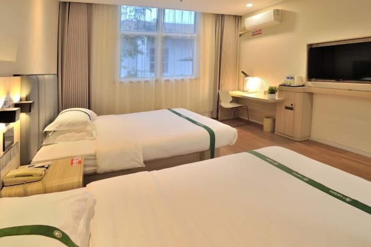 A hotel room with two single beds, a desk with a chair, a TV, and a window with curtains.