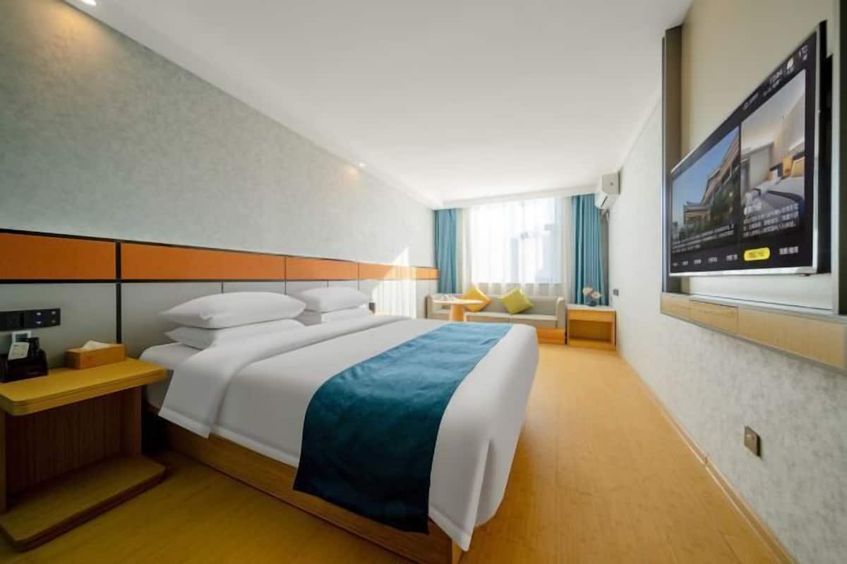 Une chambre d’hôtel avec un lit, une table de chevet, une lampe, une télévision et une fenêtre avec des rideaux.