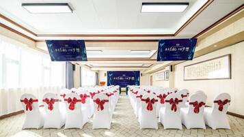 A conference room with rows of white chairs tied with red ribbons, a large screen at the front, and banners on the walls.