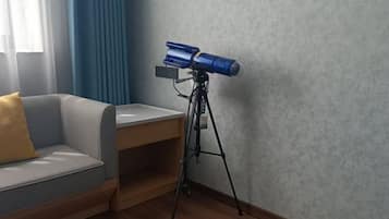 A room with a sofa, a telescope on a tripod, and a wooden side table.