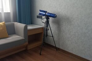 Una habitación con un sofá, un telescopio sobre un trípode y una mesita de madera.
