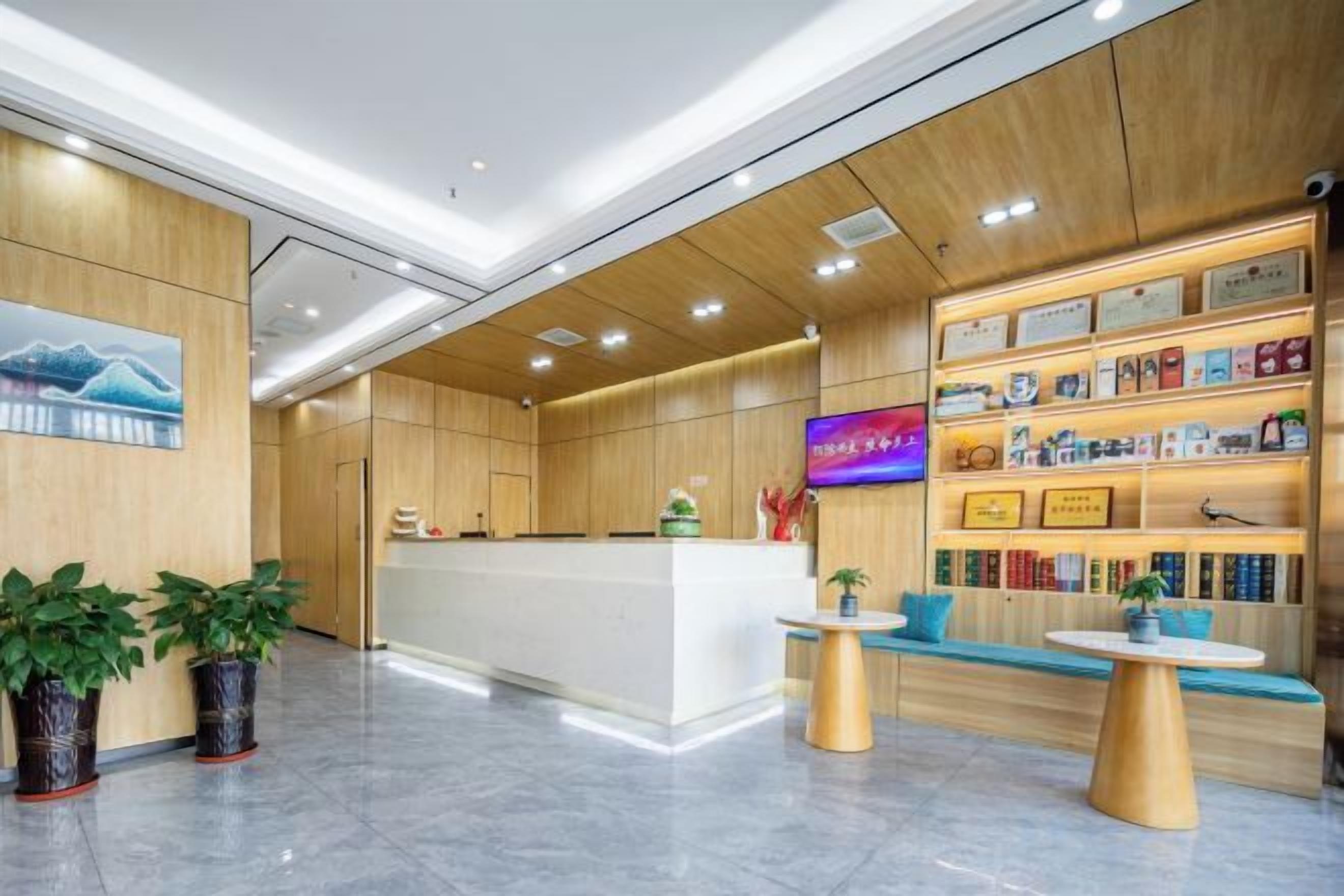 Zona de recepción de hotel con un mostrador de madera, un área de estar con una mesita y una pared con estantes que exhiben diversos objetos.