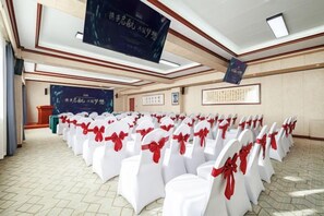 Un salón de conferencias con filas de sillas blancas, cintas rojas, una pantalla grande y un atril.