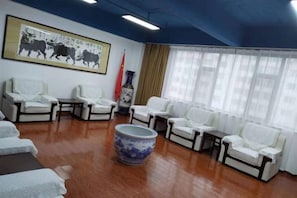 Habitación con sofás de cuero blanco dispuestos alrededor de una mesa central, un jarrón grande y un cuadro en la pared.