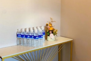 Una mesa blanca con un marco dorado, una hilera de botellas de agua y un florero con flores.