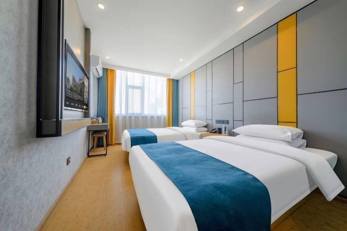 Une chambre d’hôtel avec deux lits, un téléviseur fixé au mur, un bureau et une fenêtre avec des rideaux.